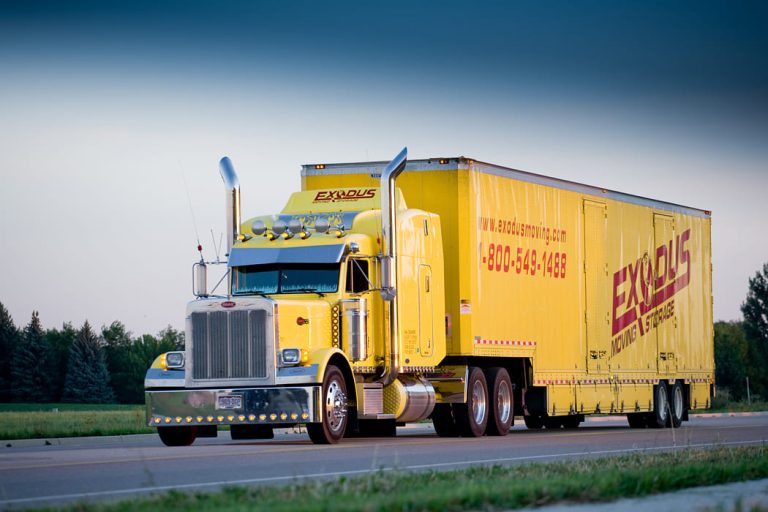 Yellow semi-truck and trailer labeled "EXODUS" on a highway.