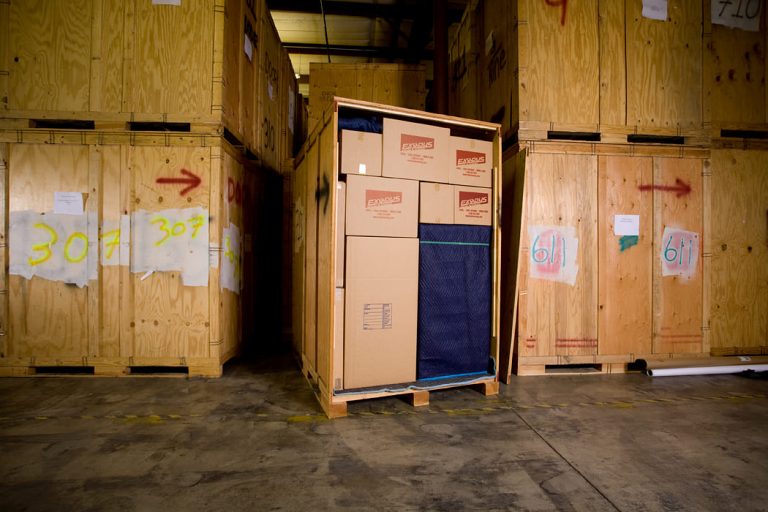 Open wooden crate with boxes inside, surrounded by other marked crates in a storage facility.