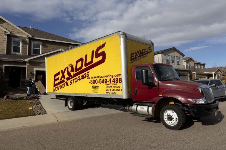 A yellow Exodus Moving Storage truck parked on a residential street with a person moving boxes.