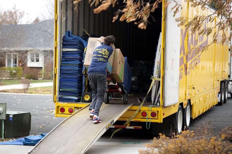 Person pushing boxes up a ramp into a yellow moving truck.