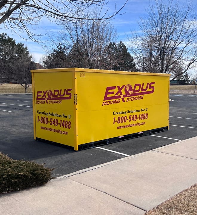 Yellow Exodus Moving & Storage container in a parking lot with trees and grass in the background.