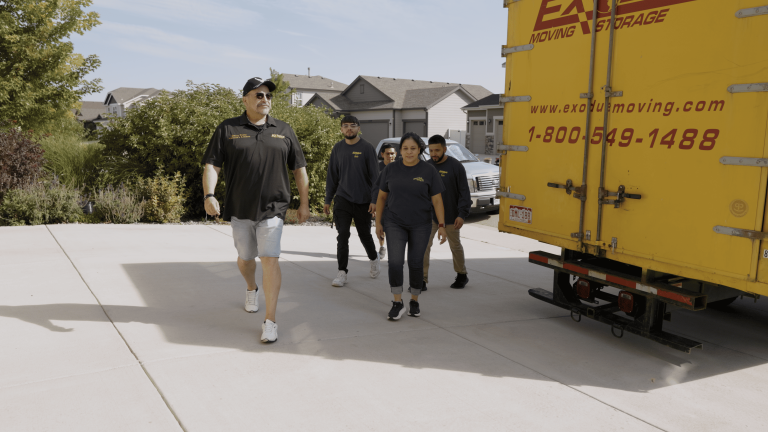 A group of five people walking past a yellow moving truck in a suburban neighborhood.