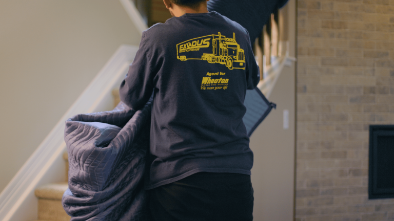 Person carrying a moving blanket, wearing a shirt with Exodus Moving & Storage logo.