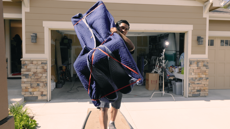 Person carrying blue padded furniture pads outside a garage.